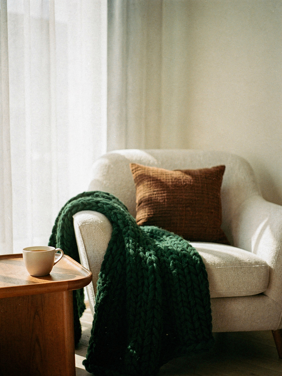 Canto de leitura com poltrona de linho, manta verde e bandeja de madeira