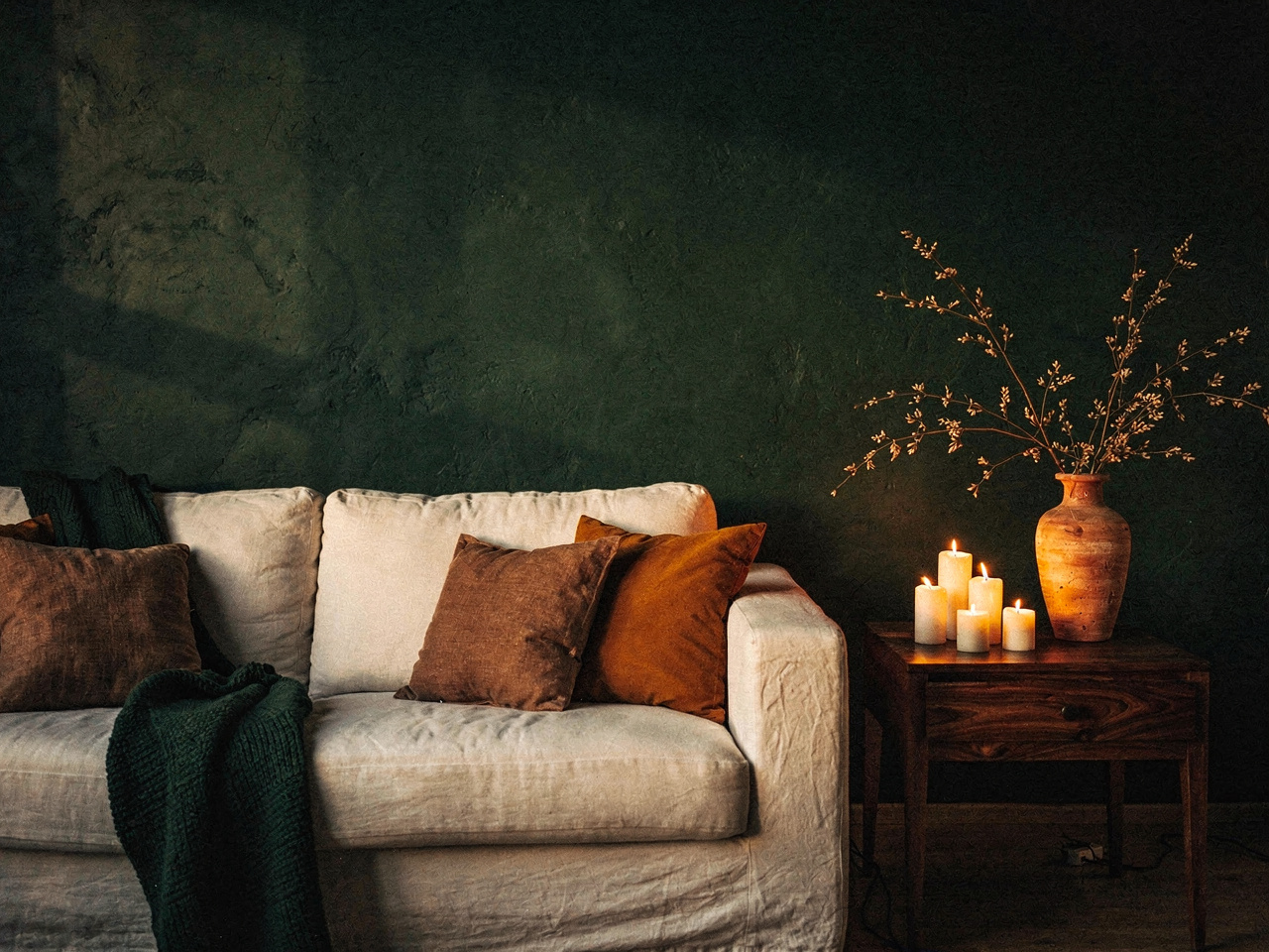 Sala em meia-luz com sofá de linho, manta verde profunda e velas acesas